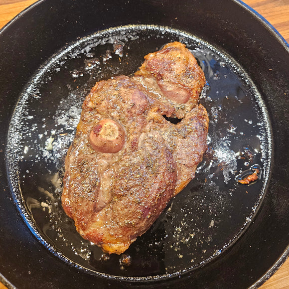 Browned lamb steak in a black cast iron skillet on a wooden surface